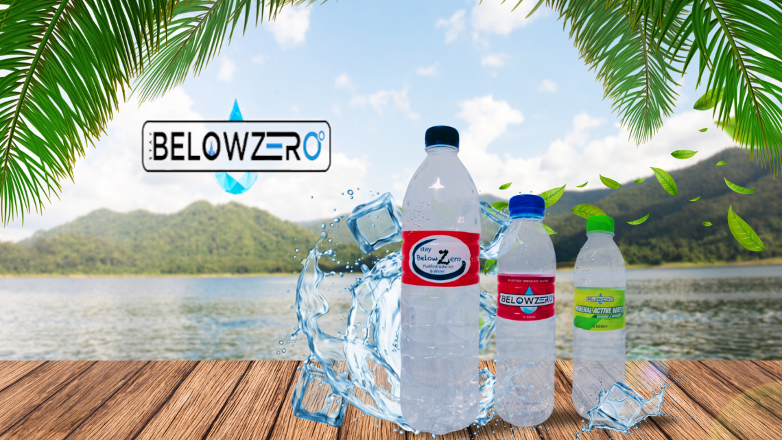 Bottles of Stay Below Zero purified water displayed on a wooden table with ice cubes, tropical leaves, and a scenic lake view in the background.